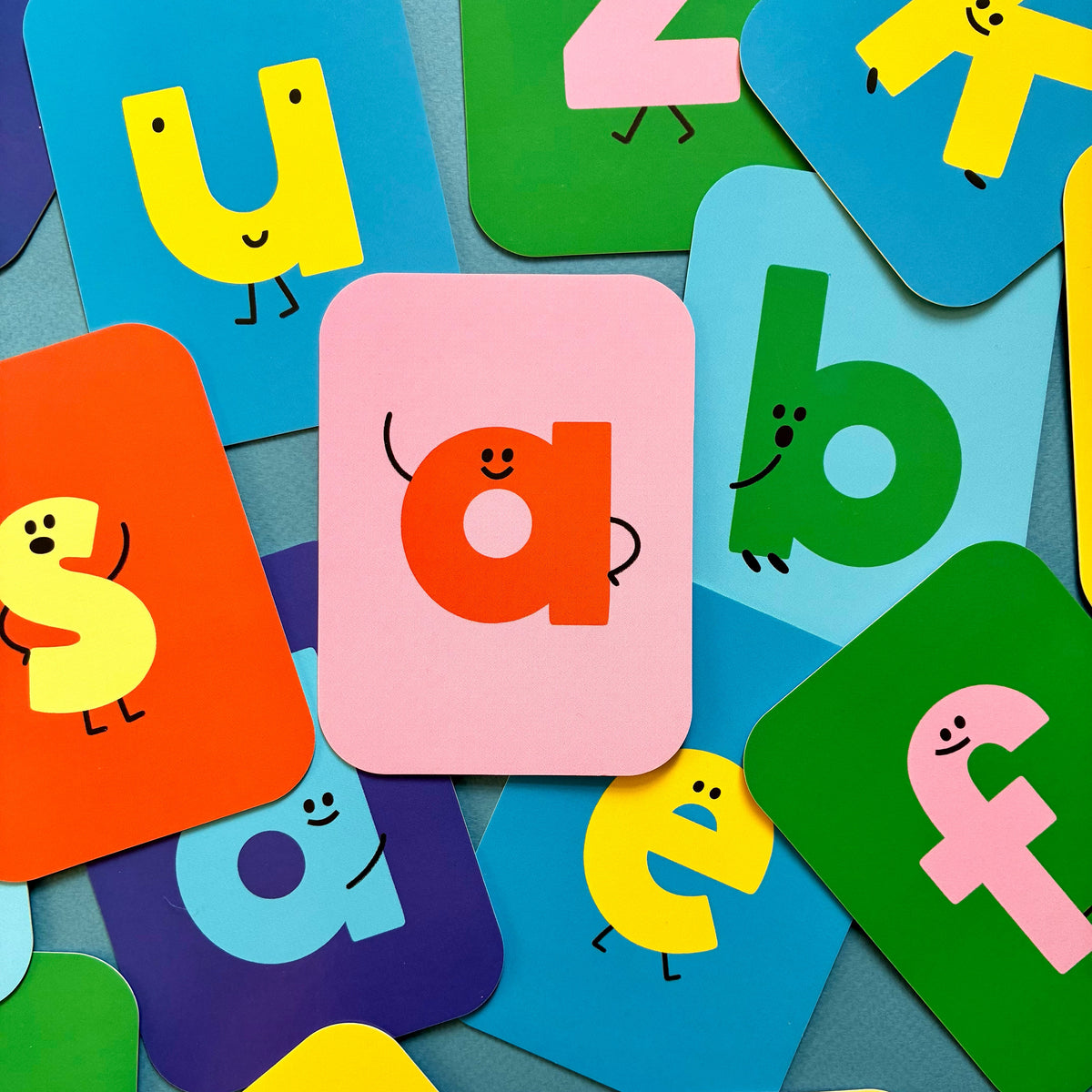 Colorful ABC Flashcards letter cards spread across a blue surface, including lowercase a, b, c, d, e, and f.