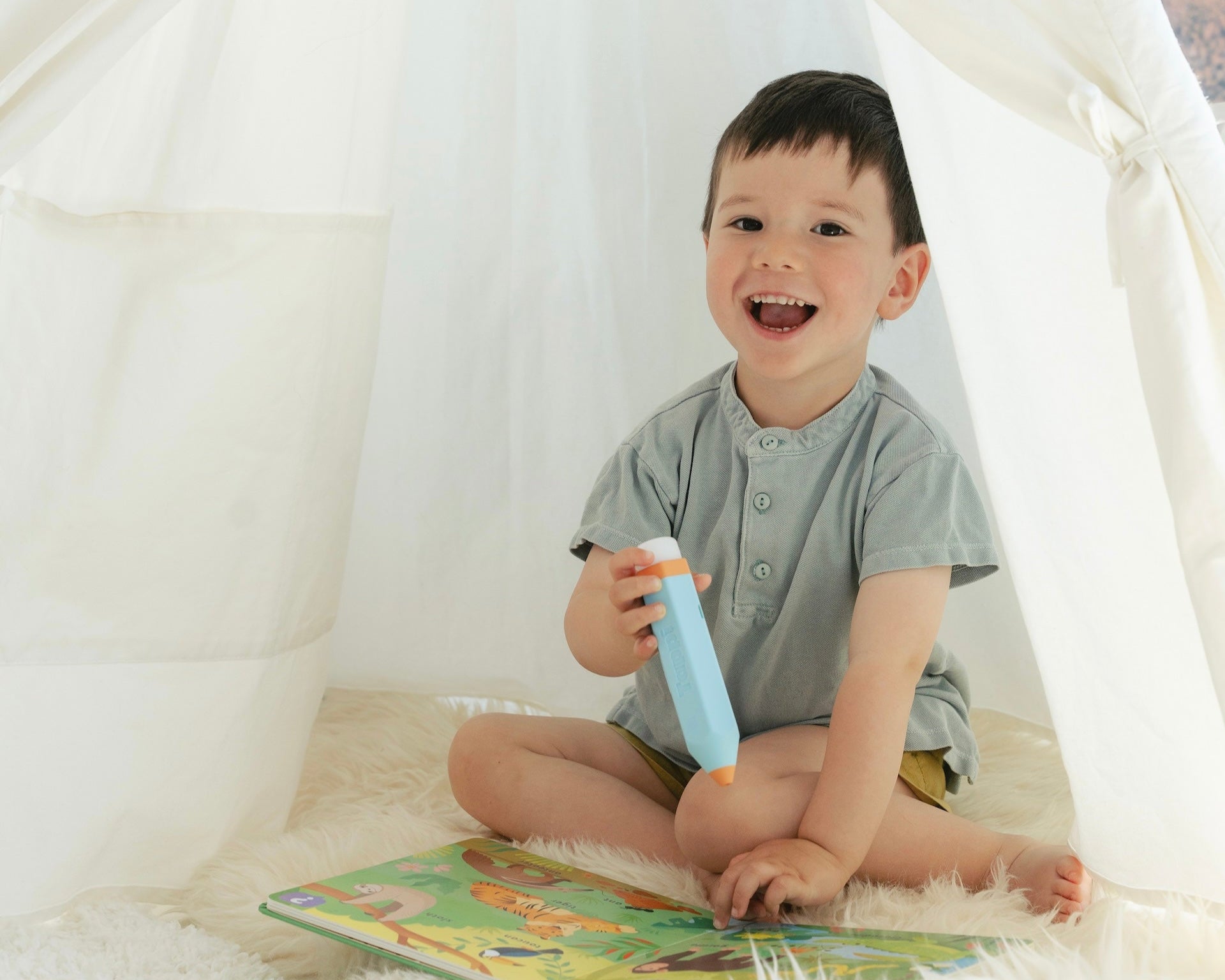 Child sitting inside a white tent, holding a toy, with a book on the floor.
